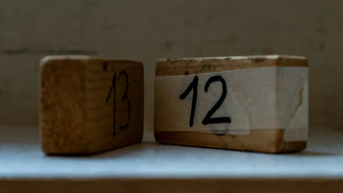 Zwei abgenutzte Holzklötze, handbeschriftet mit 13 und 12, nebeneinander auf einem Regal.